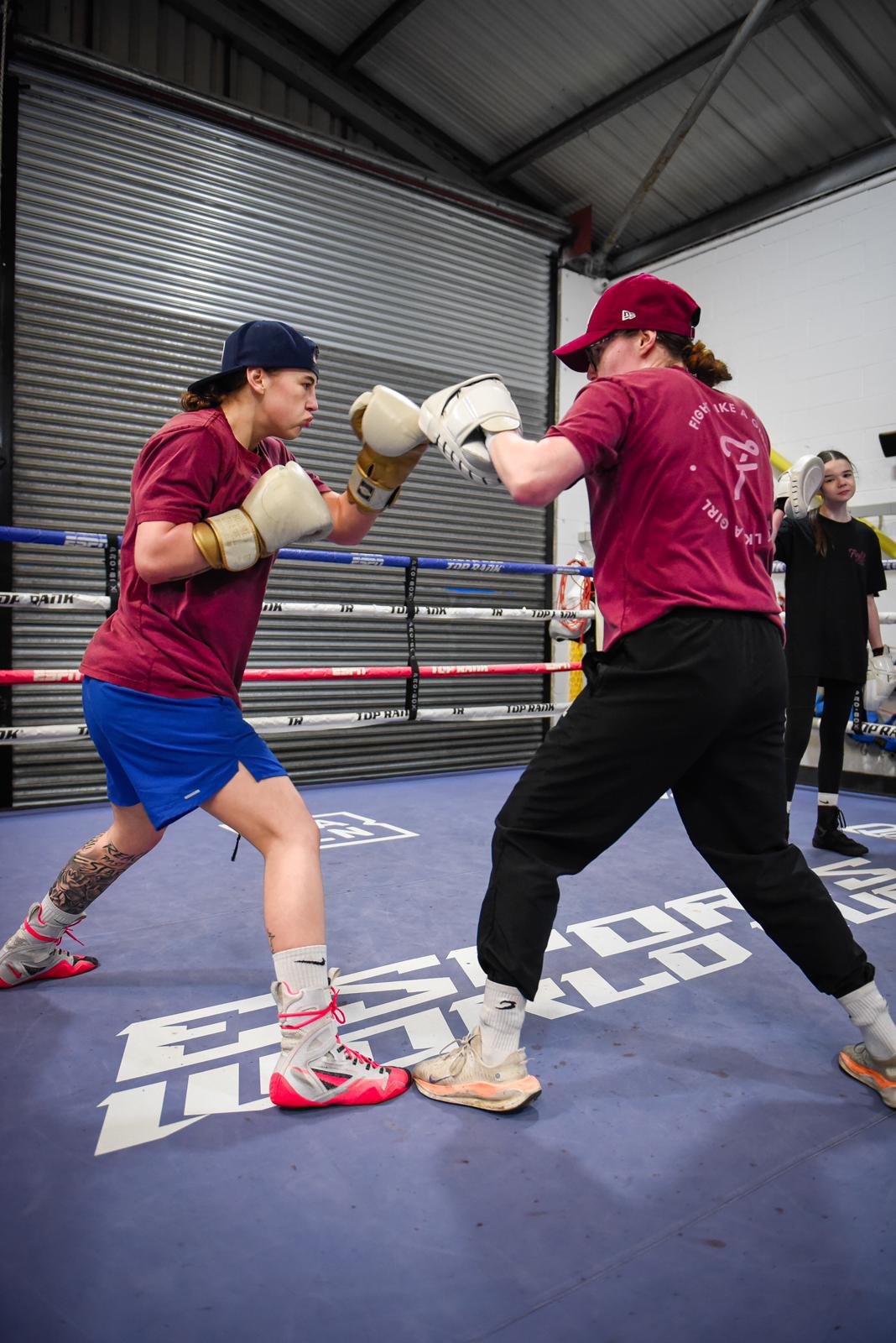 Savannah Marshall holding pads for a girl in a cap throwing a punch in a boxing ring